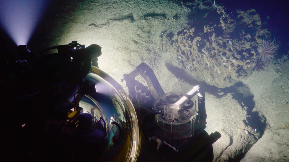 A crewed submersible working the seafloor with its manipulator arm under floodlights