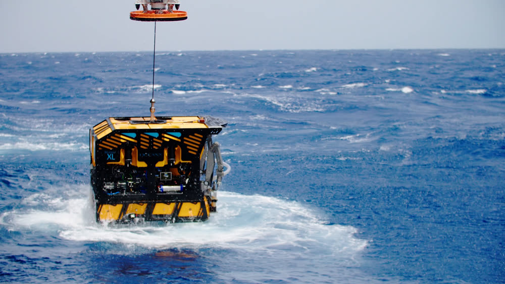 An ROV suspended from the crane, being lowered into open sea